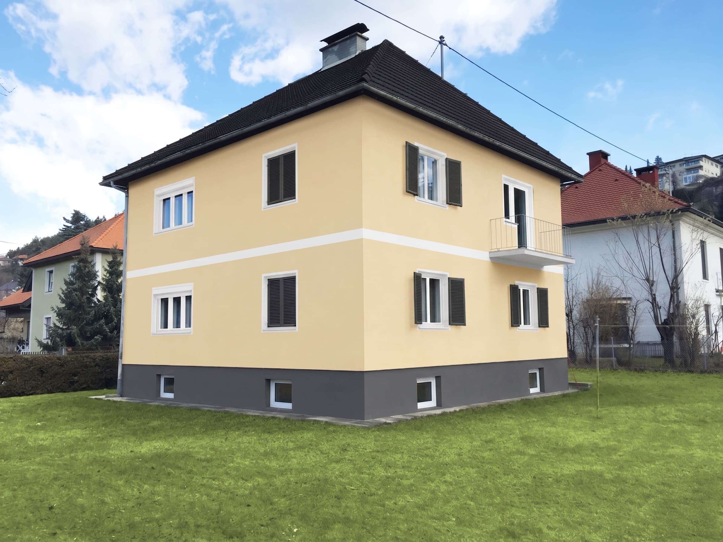 Frisch gestrichenes Wohnhaus in Sandgelb mit weißem Zierband und grauem Sockel