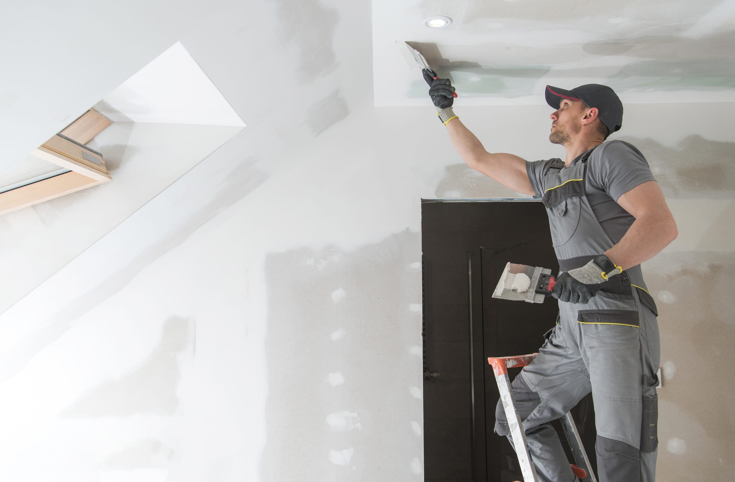 Handwerker verspachtelt die Fugen einer Gipskartondecke unter der Dachschräge
